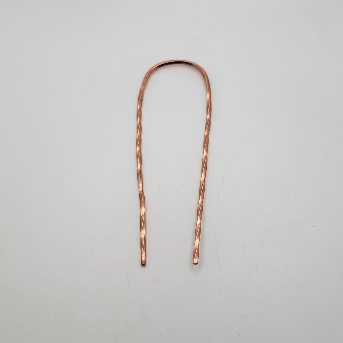 A single copper hair pin with twist design on a white background