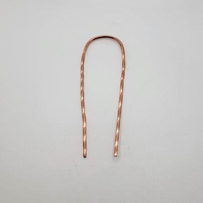 A single copper hair pin with twist design on a white background