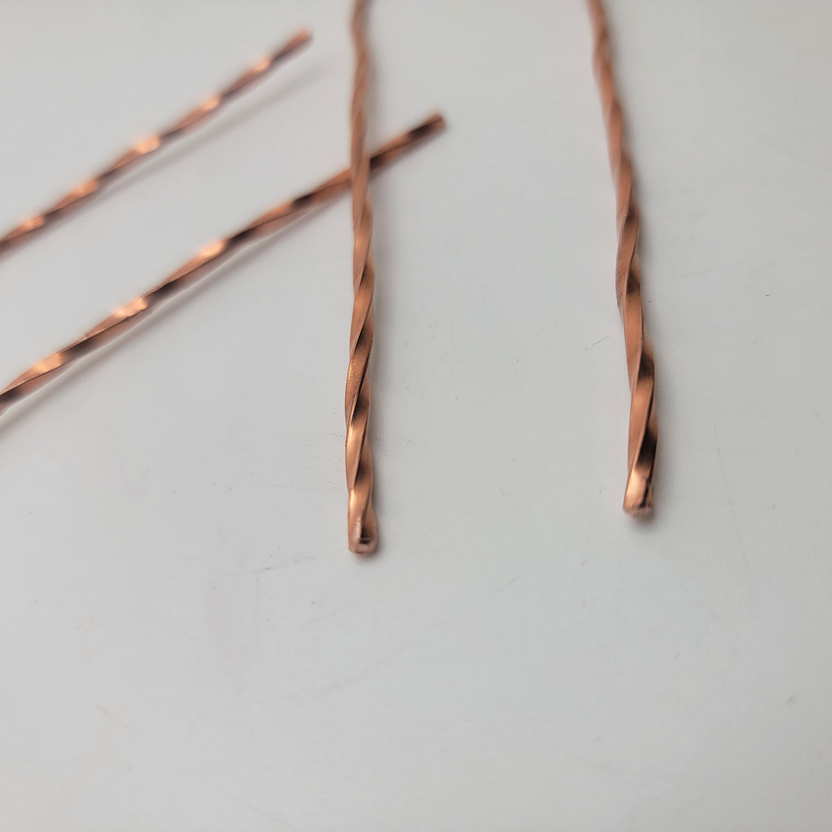 A close up of the ends of a copper hair pin with twist design on a white background