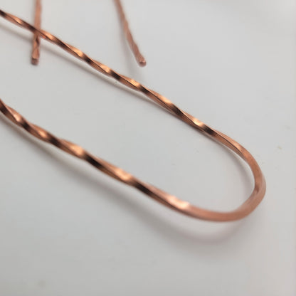 A close up of the u shaped end of a copper hair pin with twist design on a white background
