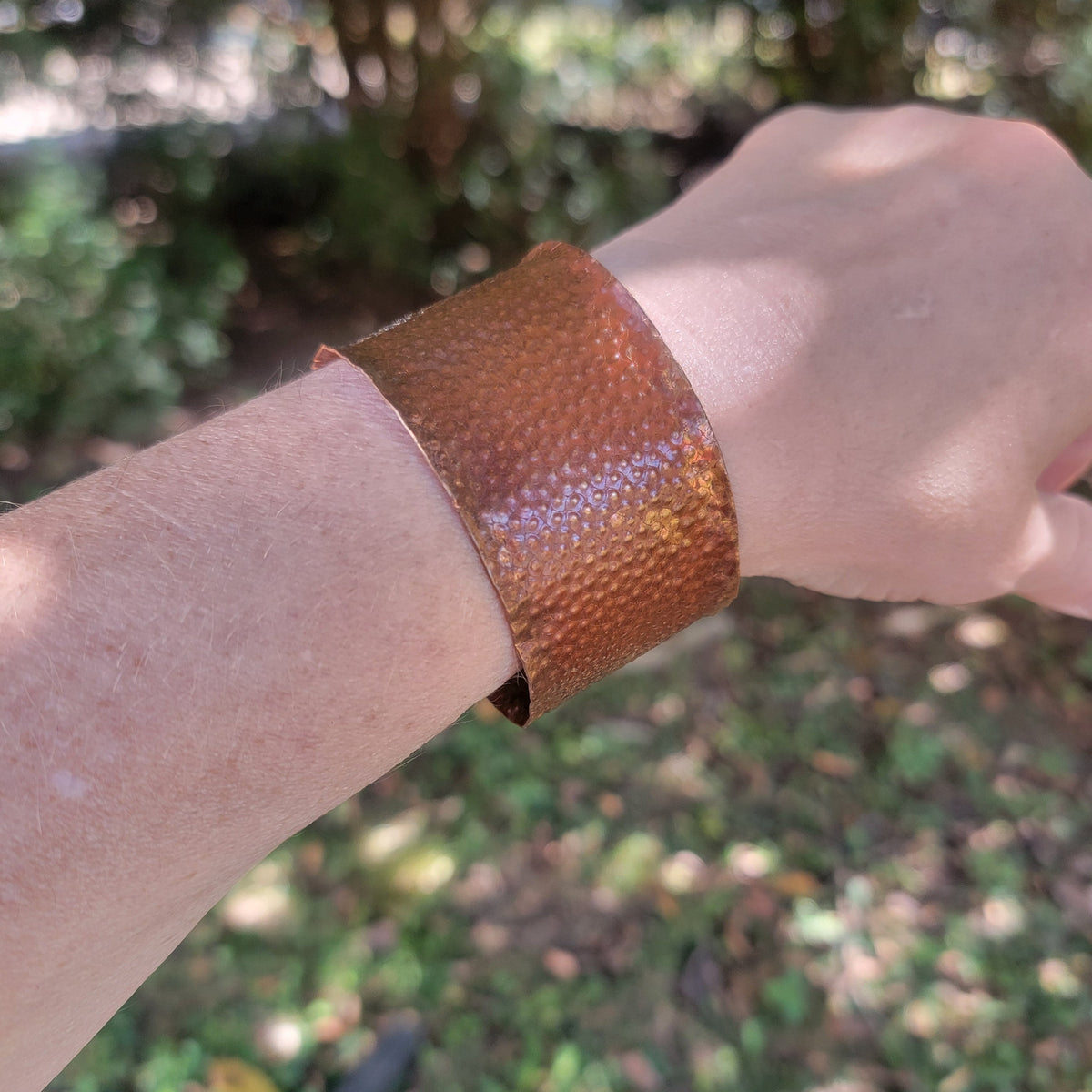 Wide textured copper cuff worn on a wrist outdoors.
