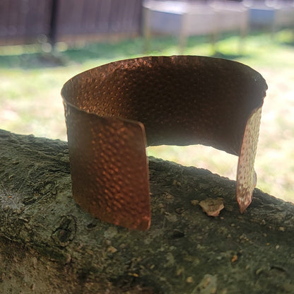 Rear angled view of wide copper cuff resting outdoors.
