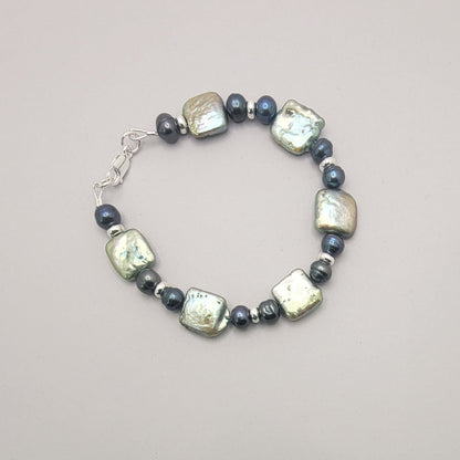 A beaded bracelet featuring baroque pearls and small dark pearls, arranged in a circle on a neutral gray background.