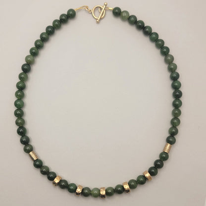 Full view of a green jade bead necklace with bronze accents and a gold-filled toggle clasp on a light background.