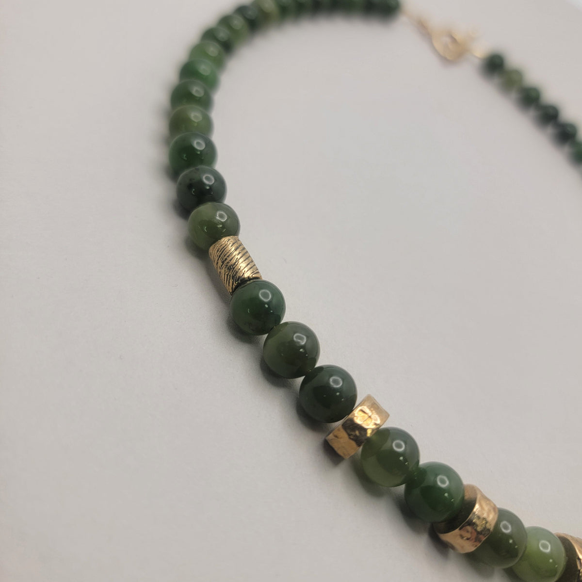 Close up view green jade bead necklace with bronze accents and a gold-filled toggle clasp on a light background.