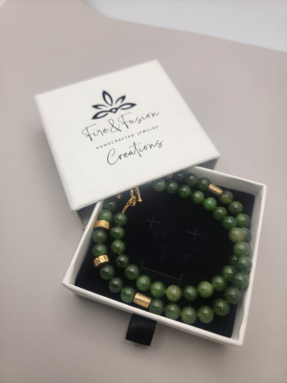 Green jade and bronze necklace displayed inside an open Fire & Fusion jewelry box.