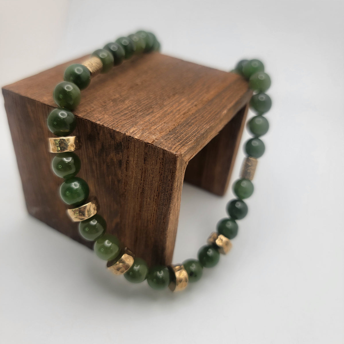 Green jade necklace draped over a wooden display block, showing textured bronze accent beads.