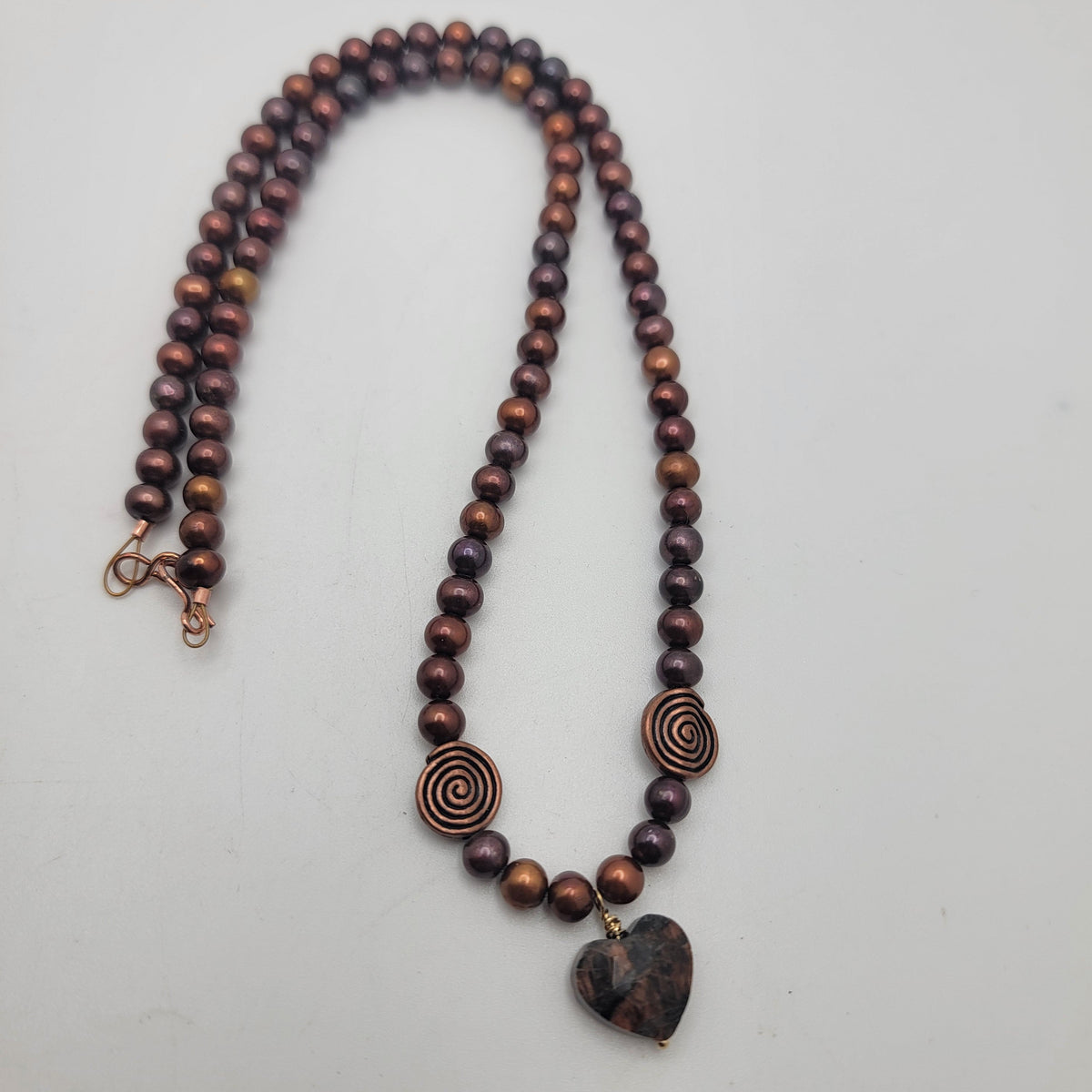 Full view of the rust pearl necklace with copper swirl beads and a heart-shaped feldspar focal on a light background.