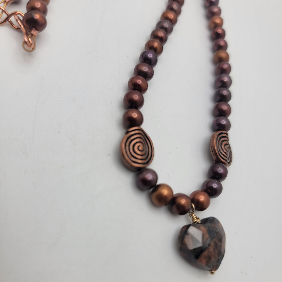 Close view of the faceted feldspar heart, gold-filled wire wrap, copper swirl beads, and rust-colored pearls.