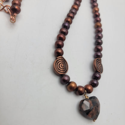 Close view of the faceted feldspar heart, gold-filled wire wrap, copper swirl beads, and rust-colored pearls.