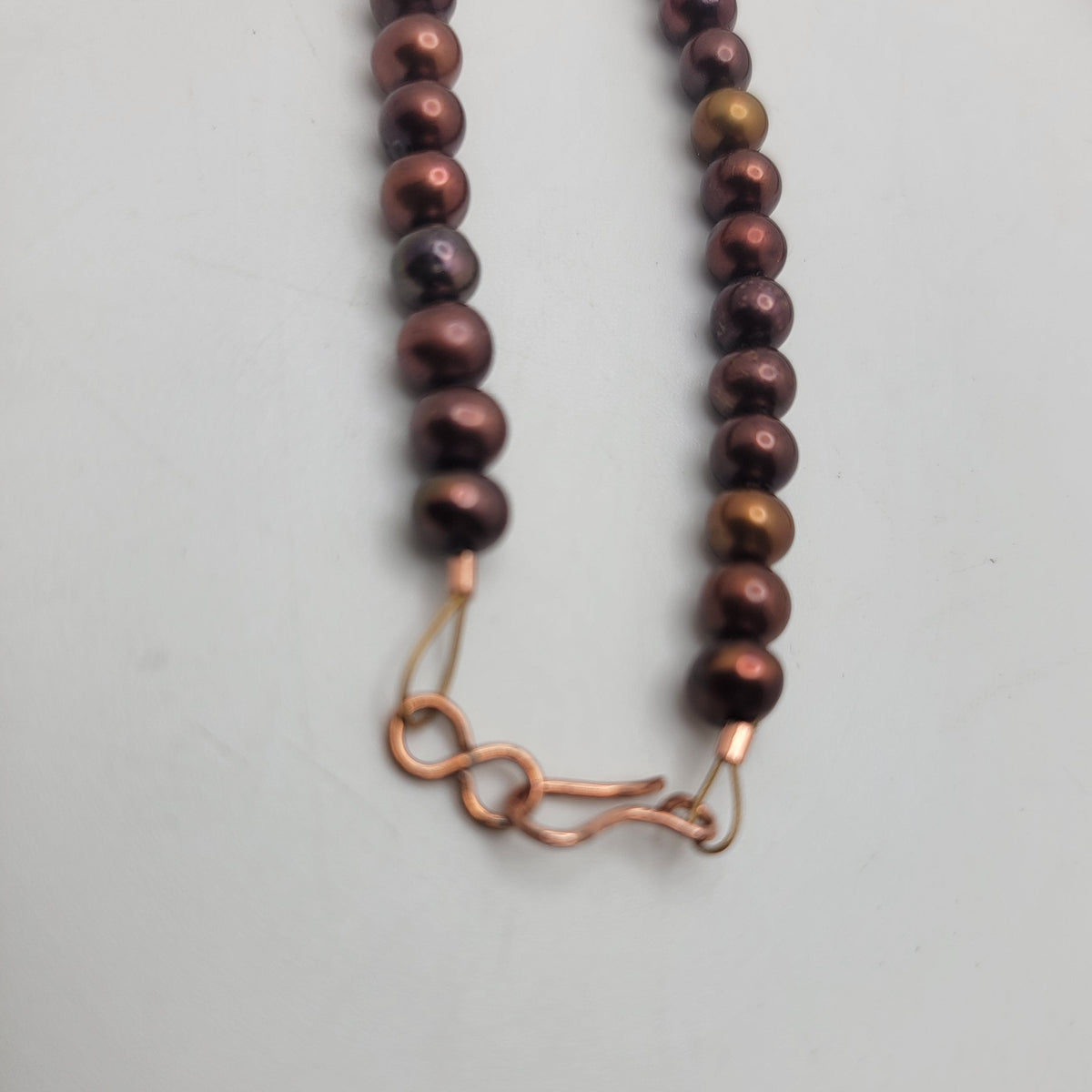 Close view of the copper S-hook clasp and rust-colored pearls.