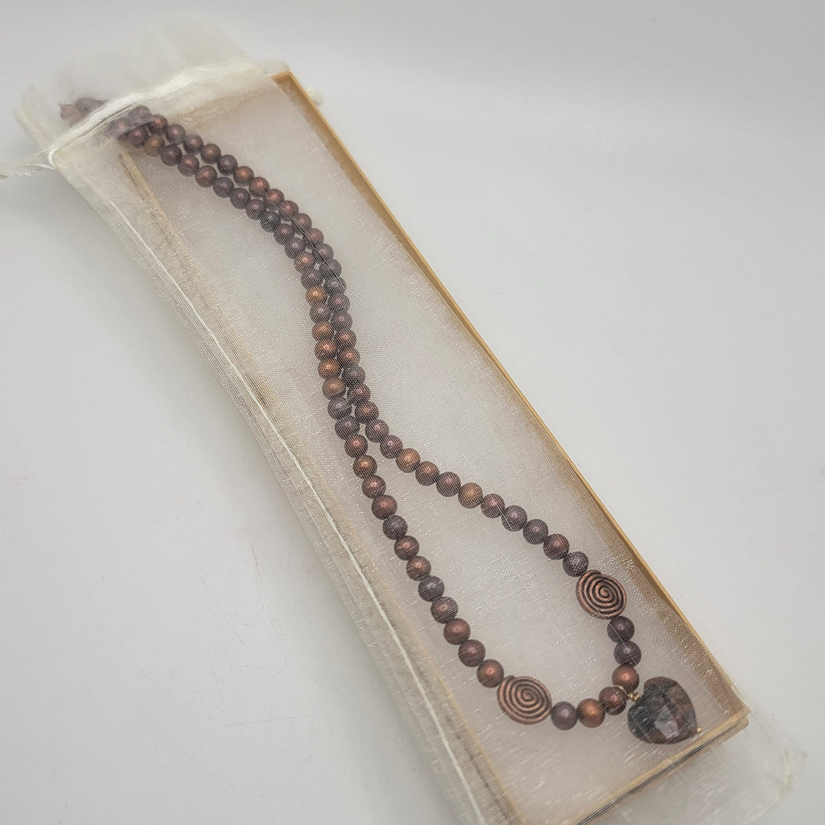 Rust pearl and feldspar heart necklace displayed in a long jewelry box.