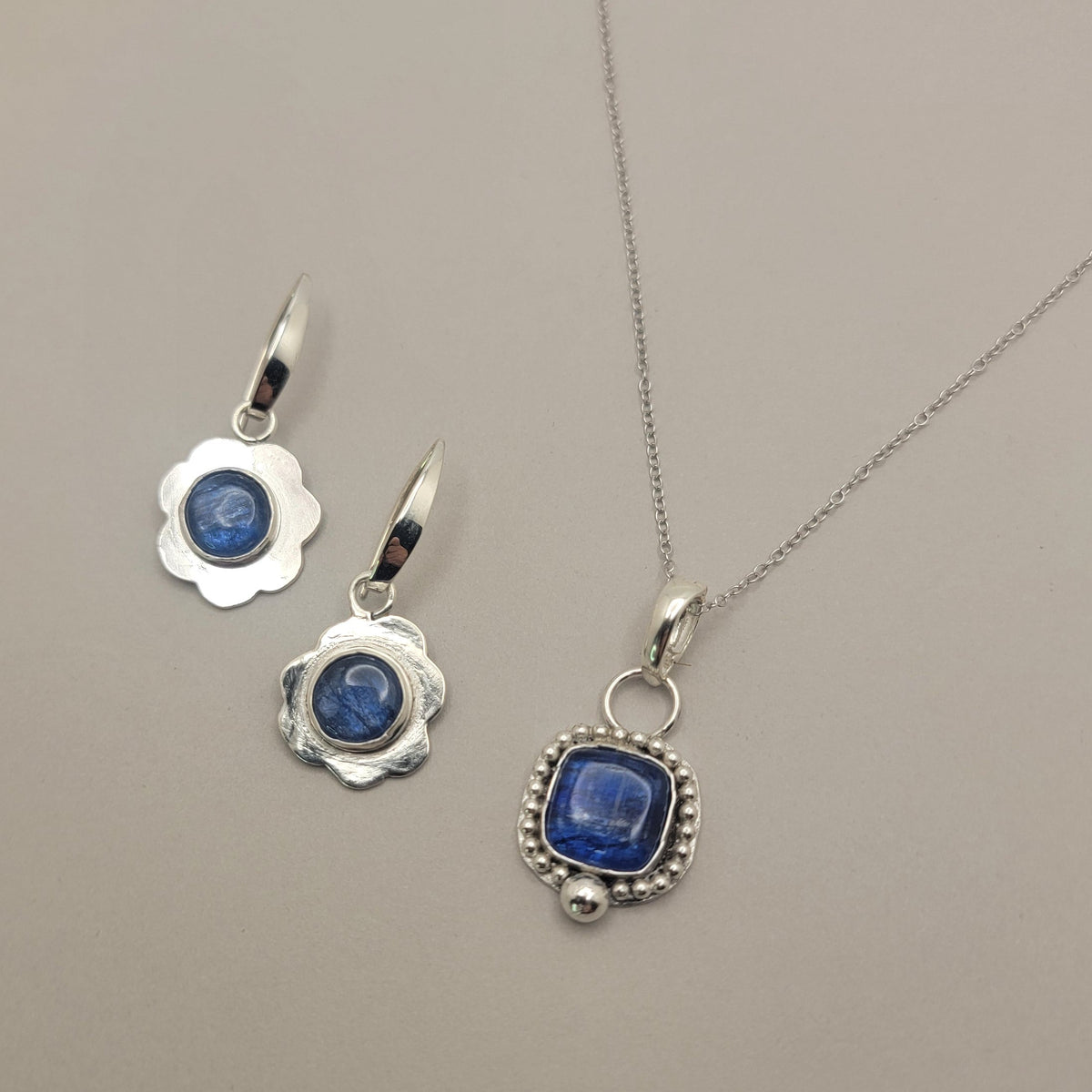 Coordinating blue kyanite sterling silver necklace and earrings arranged on a light background.