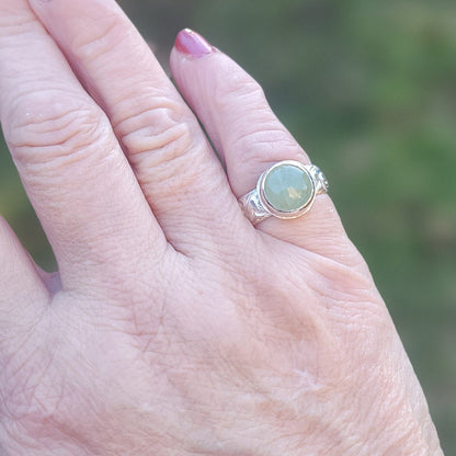 Round Aquamarine gemstone in sterling silver bezel setting with floral patterned band being shown worn on a hand in outdoor environment.
