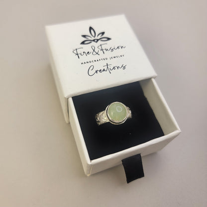 Round Aquamarine gemstone in sterling silver bezel setting with floral patterned band in a white branded gift box with the logo "Fire and Fusion Creations".