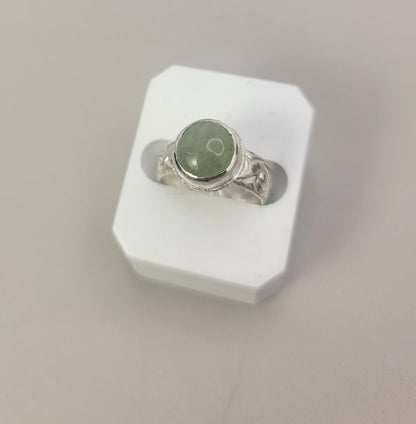Round Aquamarine gemstone in sterling silver bezel setting with floral patterned band in white display block on neutral background.