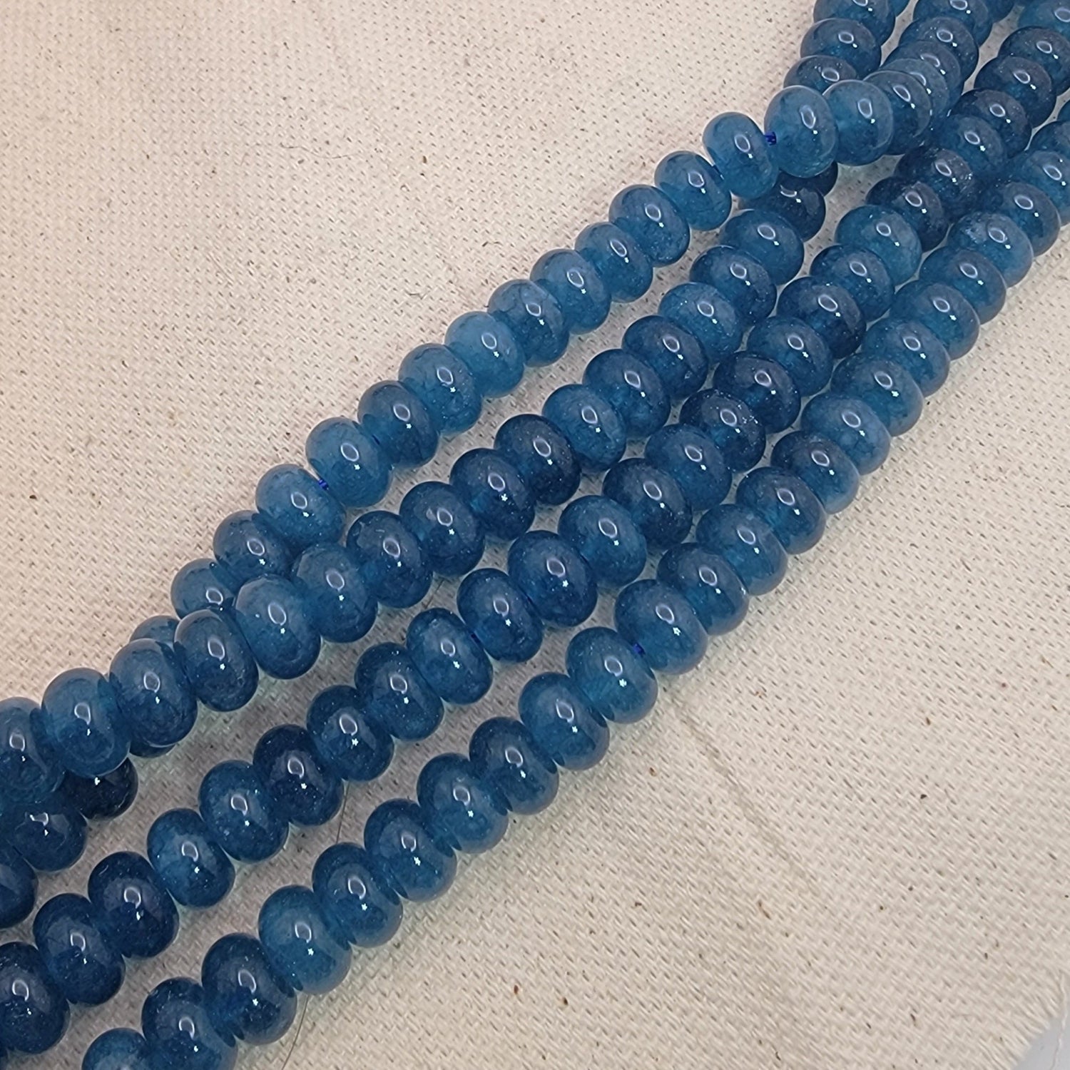 Two strands of blue kyanite gemstone beads on a textured beige surface