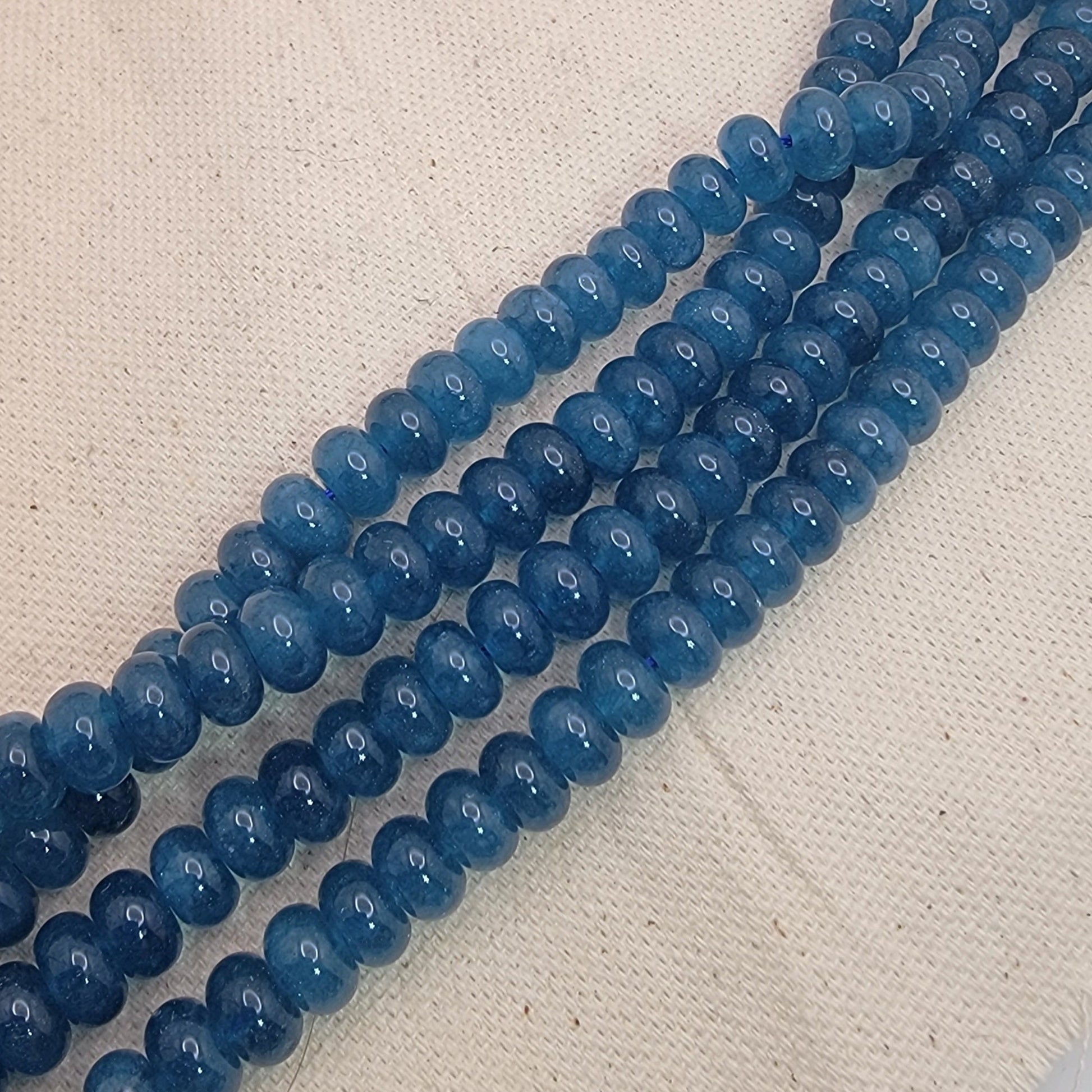 Two strands of blue kyanite gemstone beads on a textured beige surface
