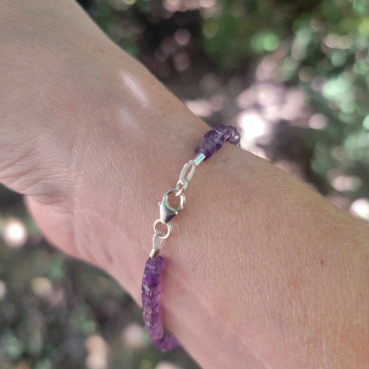 A purple beaded bracelet with a silver clasp worn on a wrist in an outdoor environment