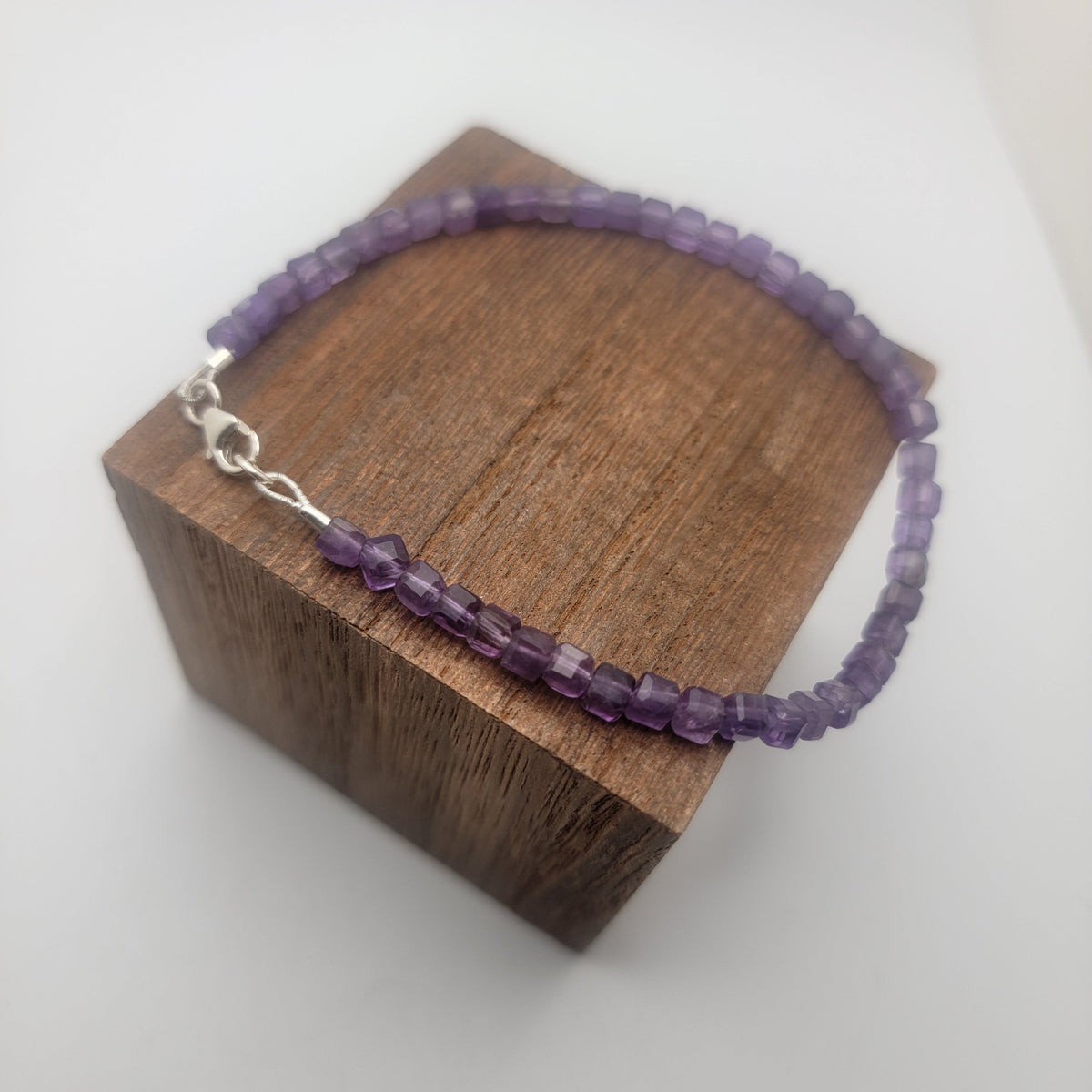 A purple beaded bracelet with a silver clasp, displayed on a dark brown wooden block against a white background.