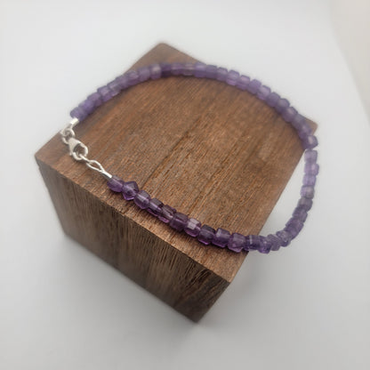 A purple beaded bracelet with a silver clasp, displayed on a dark brown wooden block against a white background.
