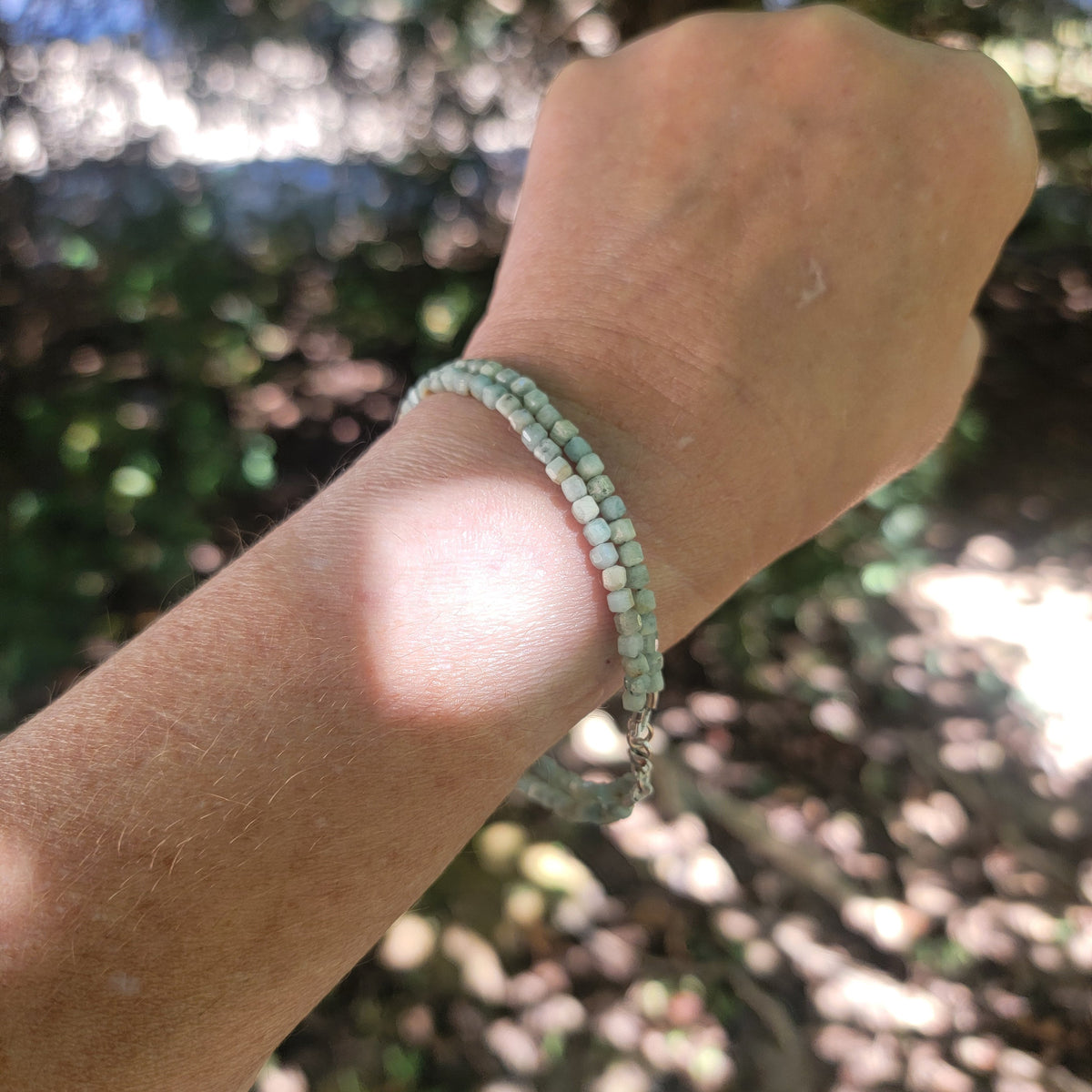 Lemurian Blue calcite beaded bracelet with sterling silver lobster clasp worn on a wrist in an outdoor environment.