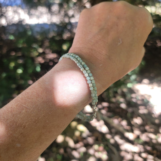 Lemurian Blue calcite beaded bracelet with sterling silver lobster clasp worn on a wrist in an outdoor environment.