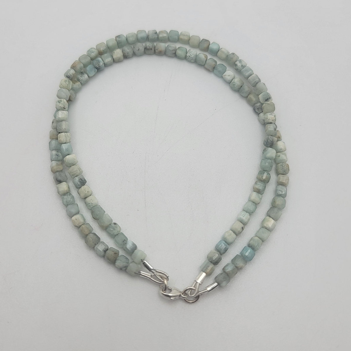 A double-strand beaded bracelet made of light blue-green stone beads with a silver clasp, displayed on a plain light gray background.