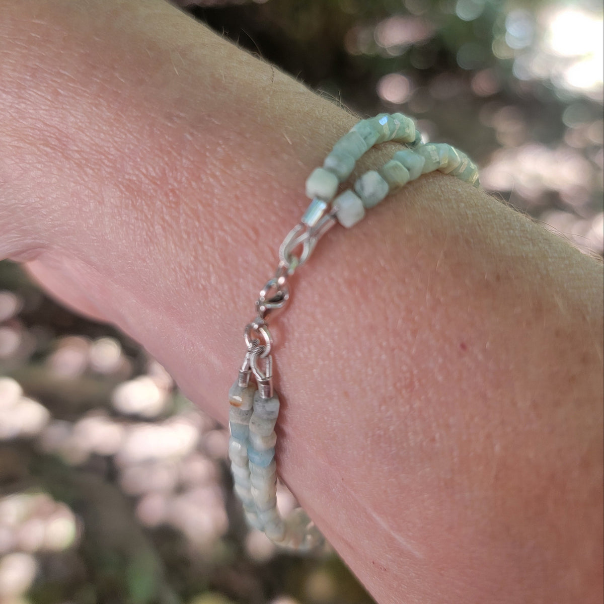 Lemurian Blue calcite beaded bracelet with sterling silver lobster clasp worn on a wrist in an outdoor environment