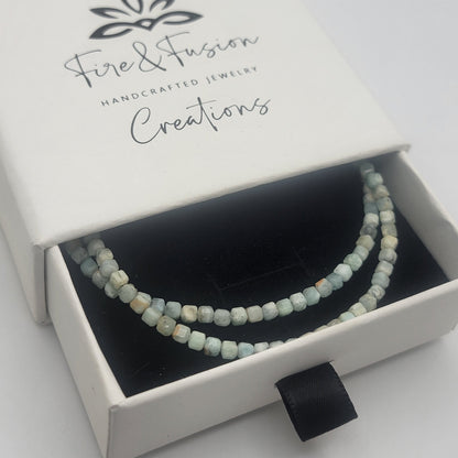 Lemurian Blue calcite beaded bracelet with sterling silver lobster clasp in a white branded gift box on a white background.