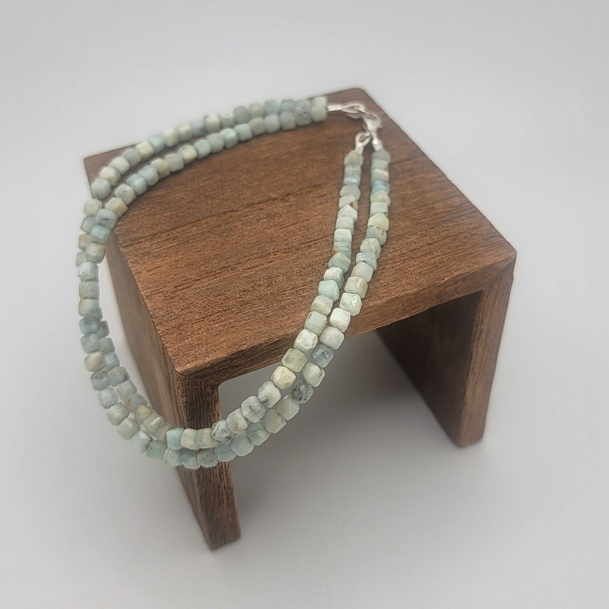 Lemurian Blue calcite beaded bracelet with sterling silver lobster clasp on a wood platform on a white background.