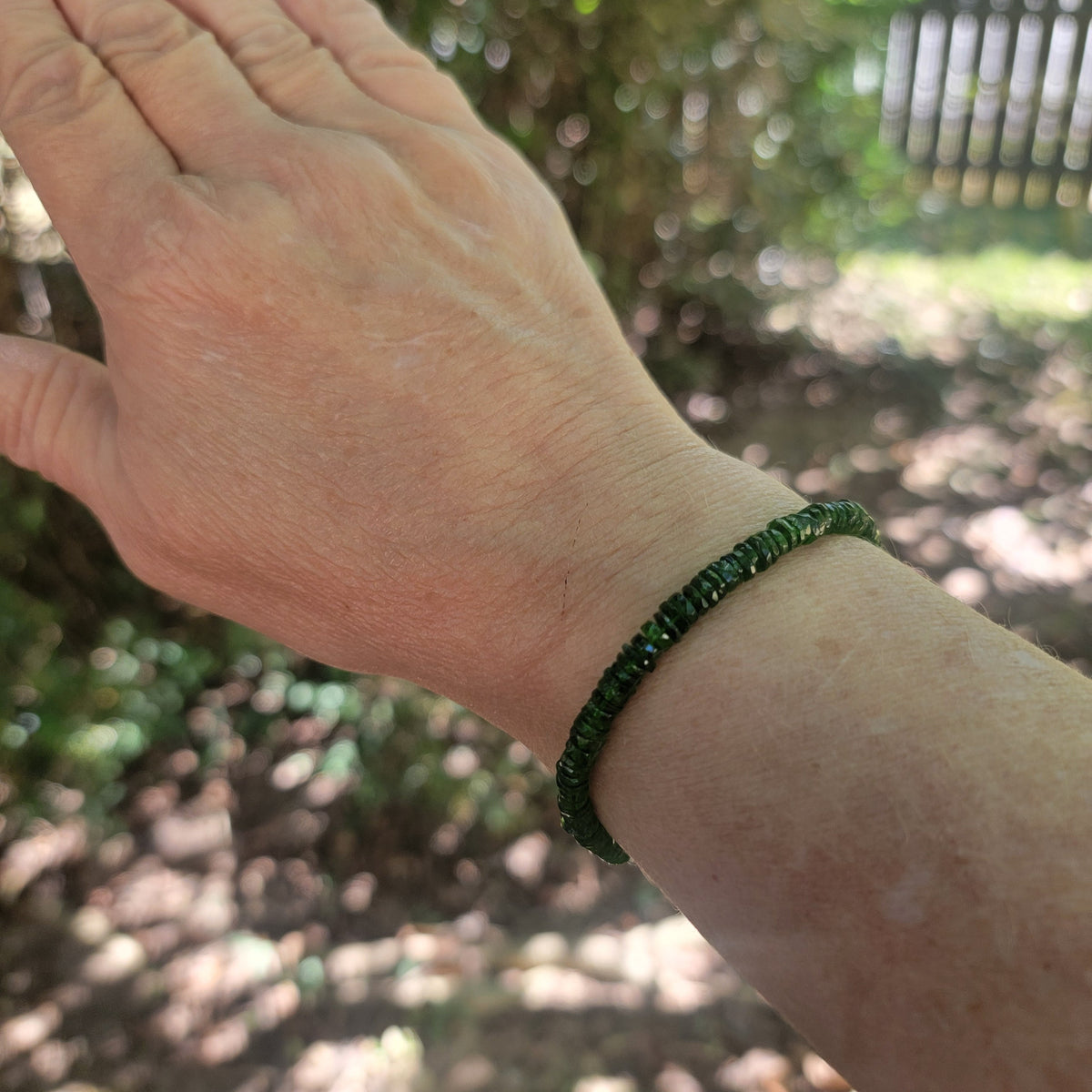 A dark green beaded bracelet worn on a person's wrist, shown in an outdoor garden setting with blurred green foliage in the background.