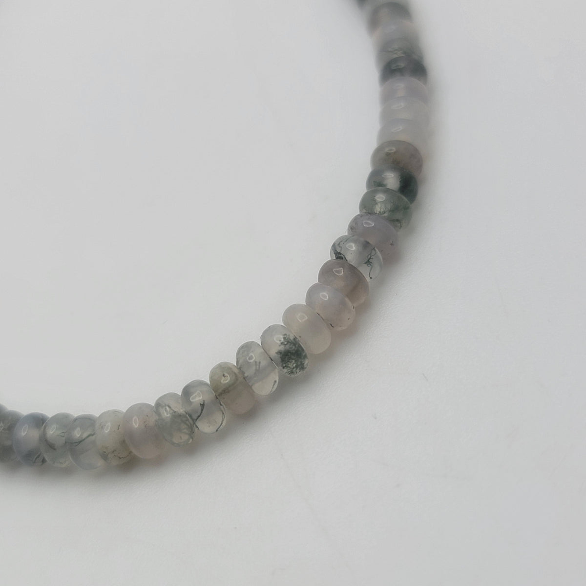 A close-up of a beaded necklace made of small, round, translucent gray beads with natural stone inclusions, photographed on a plain white background.