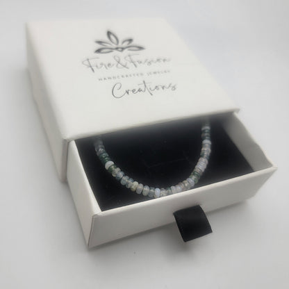 A beaded bracelet with small white and pale blue beads displayed inside an open white jewelry box. The box lid is printed with the brand name 'Fire & Fusion Creations'.