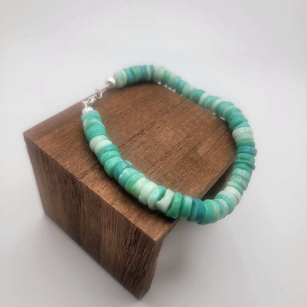 Peruvian opal beaded bracelet finished with a sterling silver lobster clasp on a wood platform on a white background.
