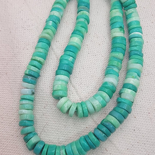Bead strands with green and blue opal beads on a textured white background