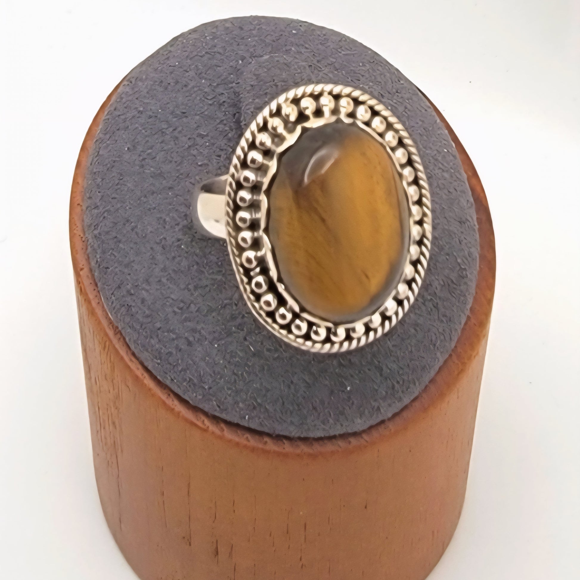 Ring with a tiger's eye stone and silver band on a wooden and gray cushioned stand.