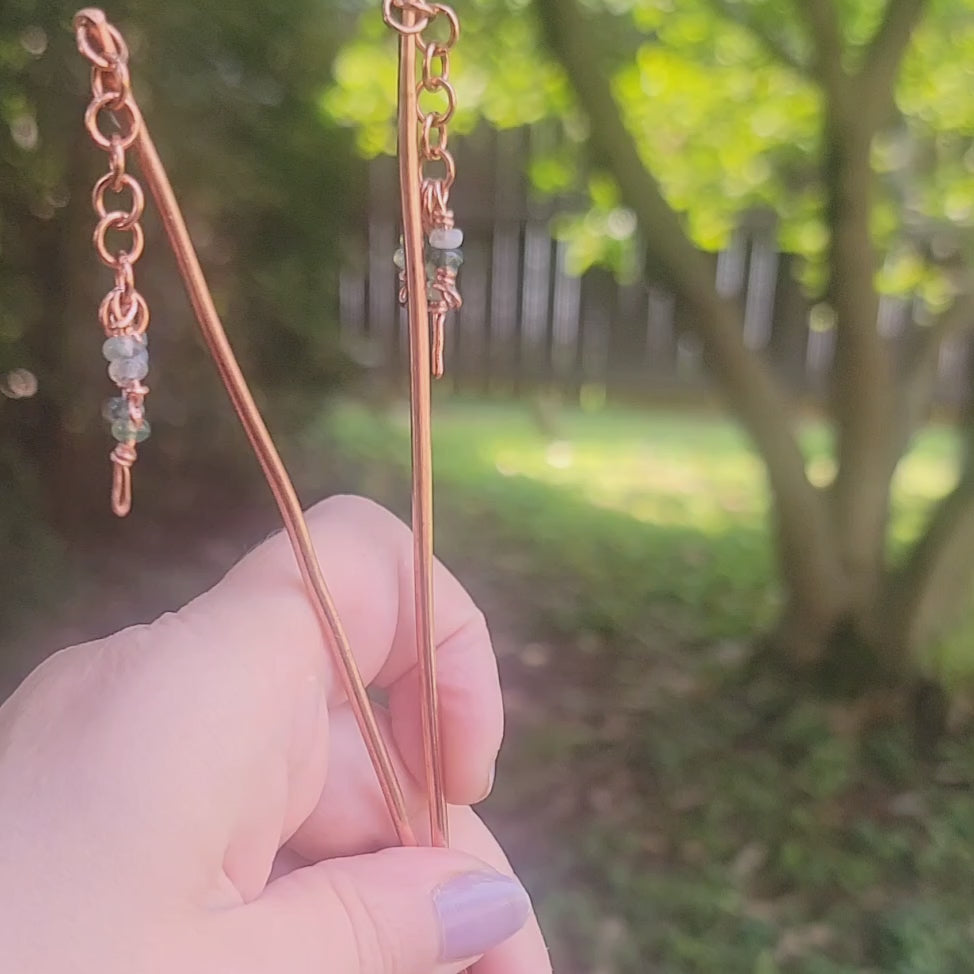 Hand holding a pair of copper beaded hair sticks against an outdoor natural background