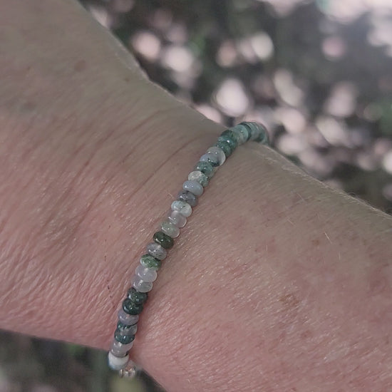 A moss agate beaded bracelet being worn on a wrist in an outdoor environment.