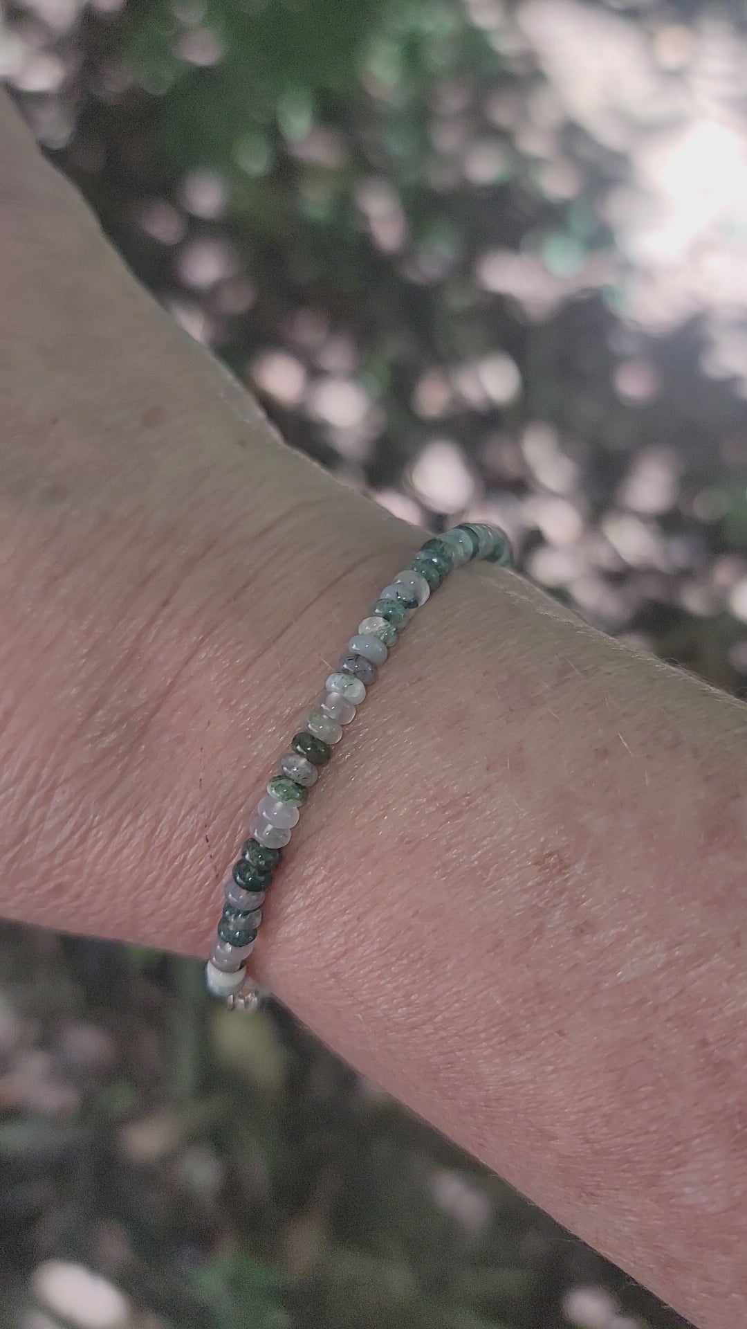 A moss agate beaded bracelet being worn on a wrist in an outdoor environment.
