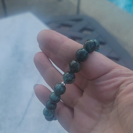 A video demonstrating a green gemstone stretch bracelet being worn on a wrist in an outdoor environment next to a swimming pool
