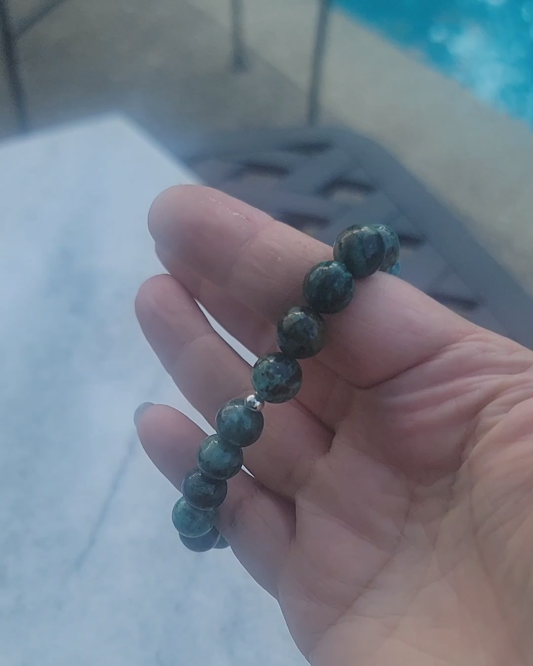 A video demonstrating a green gemstone stretch bracelet being worn on a wrist in an outdoor environment next to a swimming pool