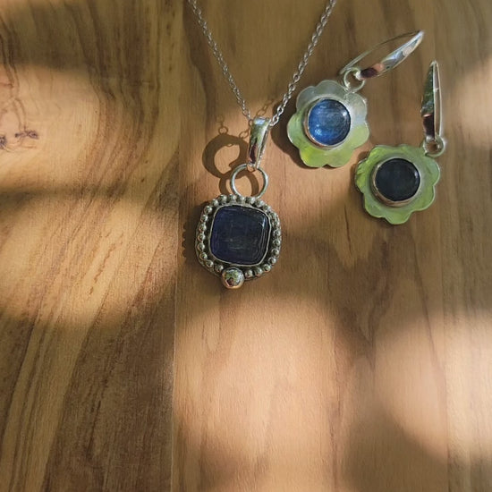 Coordinating blue kyanite sterling silver necklace and earrings on a wood platform shown outdoors.