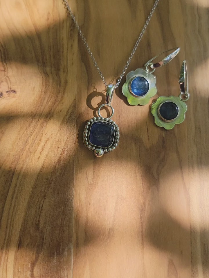 Coordinating blue kyanite sterling silver necklace and earrings on a wood platform shown outdoors.