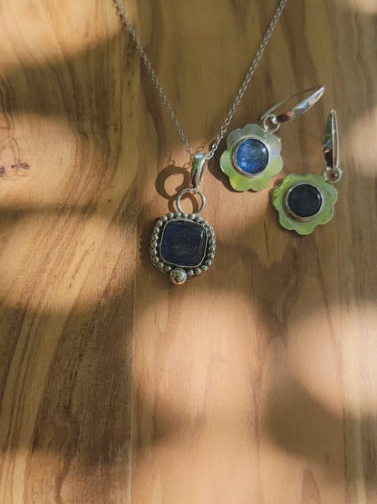 Coordinating blue kyanite sterling silver necklace and earrings on a wood platform shown outdoors.