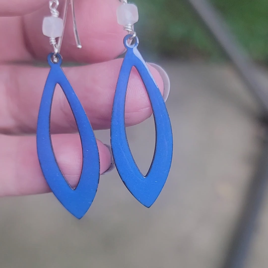 Blue earrings being held by hand against nature background