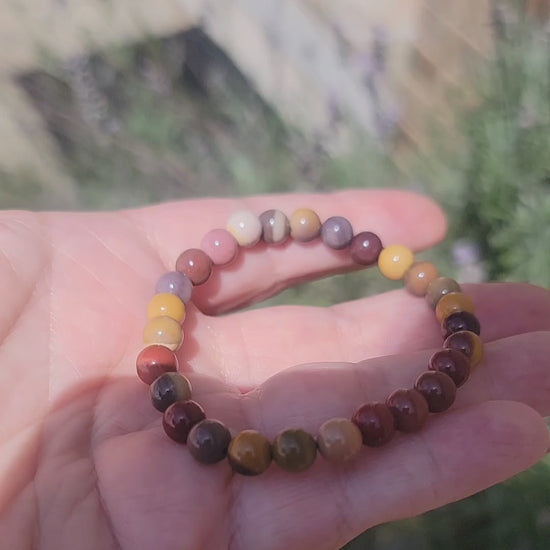 An earth tone bracelet being held in a hand outdoors