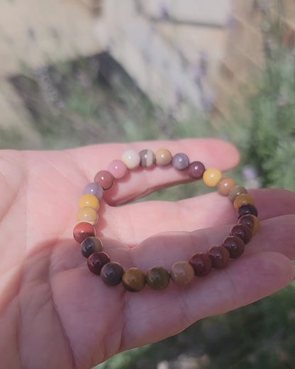 An earth tone bracelet being held in a hand outdoors