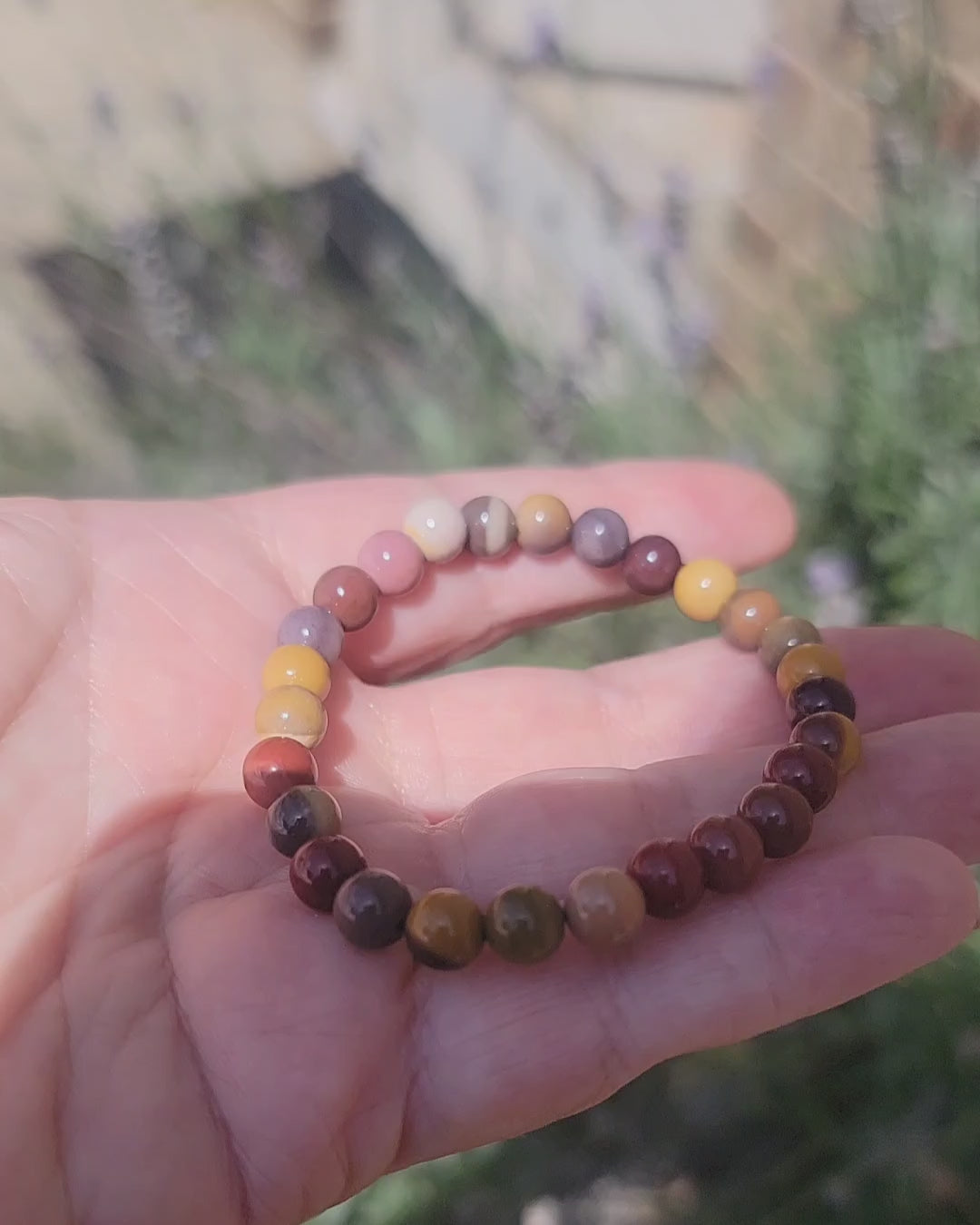 An earth tone bracelet being held in a hand outdoors