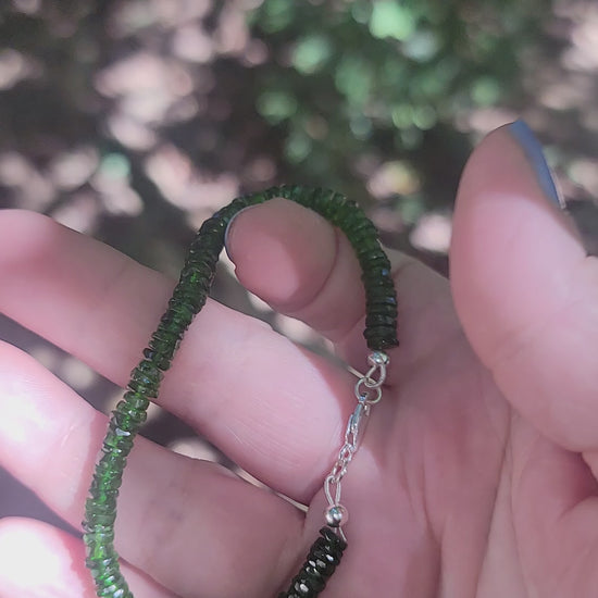 A person holding a green beaded bracelet in a hand in an outdoor environment